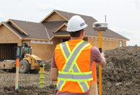 Un arpenteur effectue des mesures au GPS devant le chantier d’une maison en construction